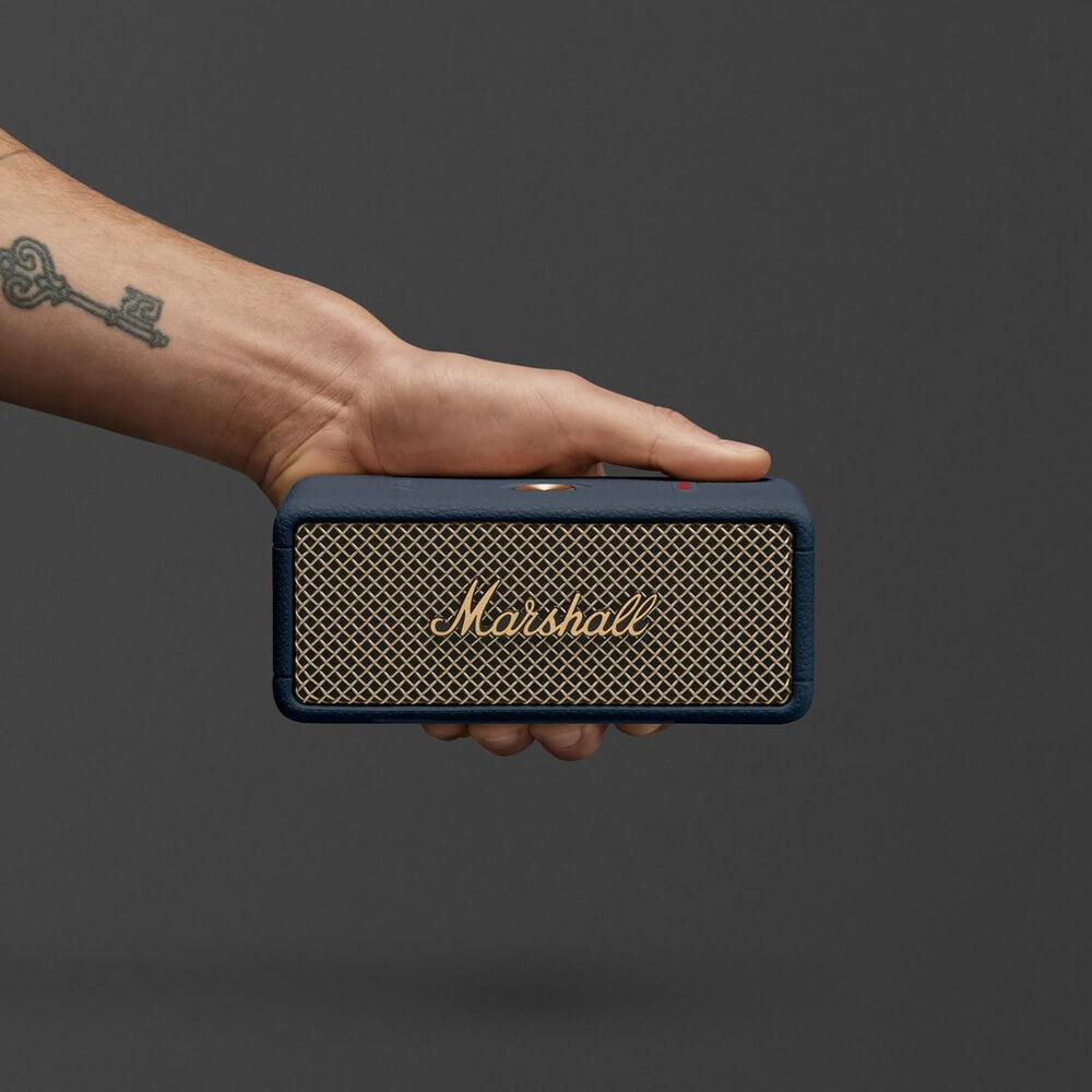 Marshall Emberton III Midnight Blue в руке — демонстрация компактности и логотипа на золотистой сетке